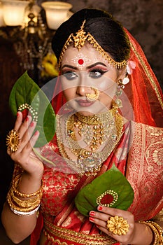 Portrait of very beautiful Indian bride holding betel leaf, Bengali bride in traditional wedding saree and makeup