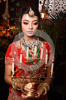 Portrait of very beautiful young attractive Indian lady in luxurious costume with makeup and heavy jewellery holding candelabra in