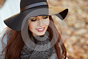 Portrait of a very beautiful young brunette woman with shiny straight hair in a gray coat and black hat smiling with downcast eye