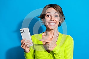 Portrait of very happy toothy smiling young lady pointing finger her new smartphone gift from boyfriend isolated on cyan