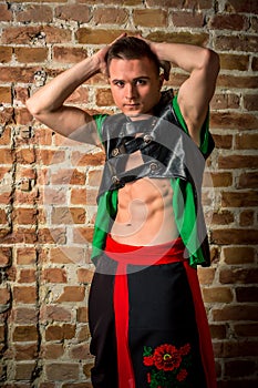 portrait of a very muscular Caucasian male model dancer in national costume against a brick wall