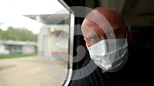 Portrait of a very sad adult bald man with a medical protective mask on his face inside a public transport. The outbreak