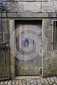 Portrait view of an ancient distressed wooden door with peeling paintwork, and a stone surround
