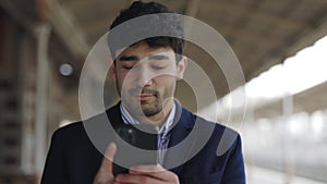 Portrait view of the busy businessman walking through the empty railway station and reading news at his smartphone while