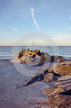 Portrait view with rocks and sandy beach in foreground of Morris Island Lighthouse