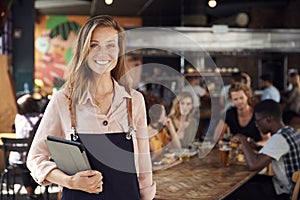 Portrait Of Waitress Holding Menus Serving In Busy Bar Restaurant