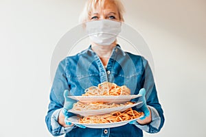 Portrait of waitress holding plates of Italian spaghetti pasta wearing protective surgical mask