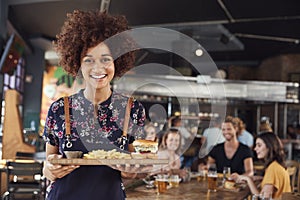 Portrait Of Waitress Serving Food To Customers In Busy Bar Restaurant photo