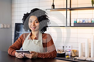 Portrait waitress of a small business owner of a cafe, woman in apron smiles and looks at camera with a tablet computer