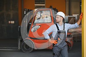 Portrait of warehouse forklift driver standing in storehouse by the machine.