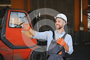 Portrait of warehouse forklift driver standing in storehouse by the machine.