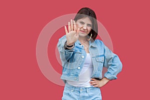 Portrait of warning beautiful brunette young woman with makeup in denim casual style standing with hand on waist and looking at