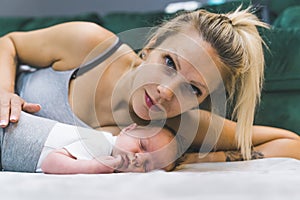 Portrait of white blond mother with lying with her infant boy on the floor caressing him and looking proudly into camera