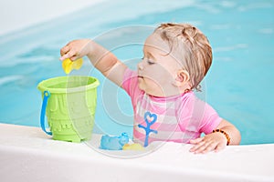 Portrait of white Caucasian baby girl playing with toys in water on swimming pool nosing inside