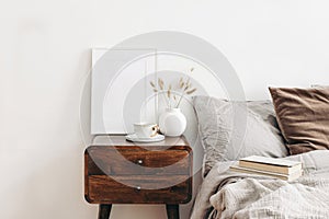 Portrait white frame mockup on retro wooden bedside table. Modern white ceramic vase with dry Lagurus ovatus grass and