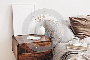 Portrait white frame mockup on retro wooden bedside table. Modern white ceramic vase, dry Lagurus ovatus grass. Cup of