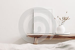 Portrait white frame mockup on vintage wooden bench, table. Modern white ceramic vase with dry Lagurus ovatus grass and