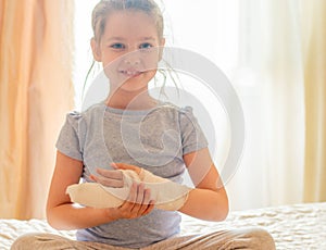 Portrait of a white girl with her arm in a cast due to an injury, wearing a blue T-shirt, sitting on the bed in her room