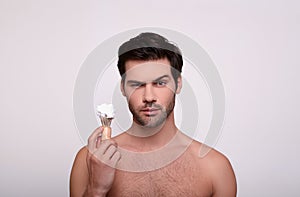 Portrait of a white handsome brunette with a beard, holding a shaving brush in his hand