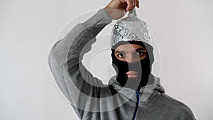 Portrait of a white man  in a black balaclava puts on a foil hat. 5G tower radiation protection.