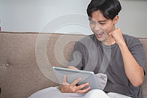 Portrait of a white man listening to music with a tablet in hand holding a pen on the sofa inside the house to relax on vacation