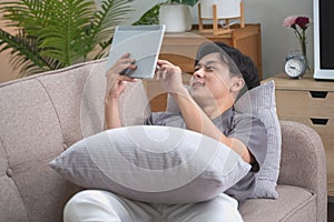 Portrait of a white man listening to music with a tablet in hand holding a pen on the sofa inside the house to relax on vacation