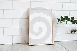 Portrait white picture frame mockup and eucalyptus on table. Brick tiles wall on background. Scandinavian, nordic style