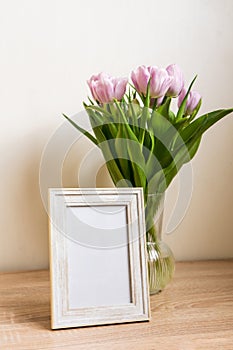 Portrait white picture frame mockup on wooden table. Modern vase with tulips.Scandinavian interior