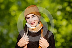 Portrait White young guy in a hat and sweater wrap neck a scarf, on green bokeh background