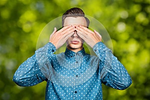 Portrait White young man dressed in blue shirt, closes eyes his hands. Man on green bokeh background