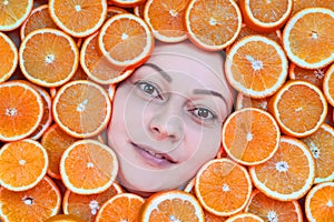 Portrait of a woman of 35 years with brown eyes on a background of sliced â€‹â€‹juicy orange oranges. Orange frame. Healthy food