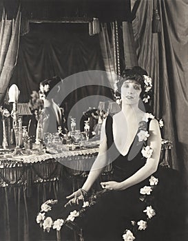 Portrait of woman adorned with flowers sitting at dressing table