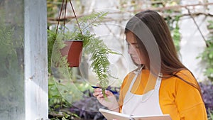 Portrait of woman agronomist near plant in pot reading her notes in notepad.