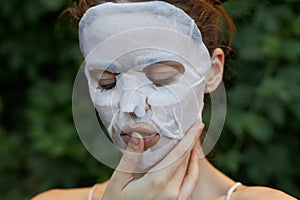 Portrait of a woman anti-aging mask holds a finger near the lips and closed eyes bare shoulders leaves in the background