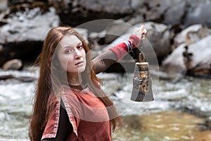 portrait of woman with an antique bell. in the hands against the background of mountain river, the concept of antiquity