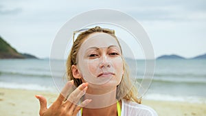 Portrait woman applying sun cream protection lotion.Woman looking at camera on beach near sea smearing sunscreen cream
