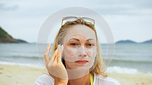 Portrait woman applying sun cream protection lotion.Woman looking at camera on beach near sea smearing sunscreen cream