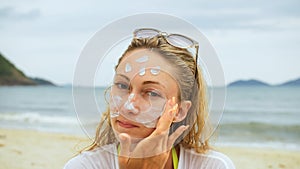 Portrait woman applying sun cream protection lotion.Woman looking at camera on beach near sea smearing sunscreen cream