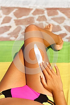 Portrait of woman applying sunscreen on legs. Close-up smooth tanned legs