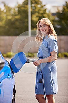 Portrait Of Woman Attaching Charging Cable To Zero Emission Electric Car Outdoors