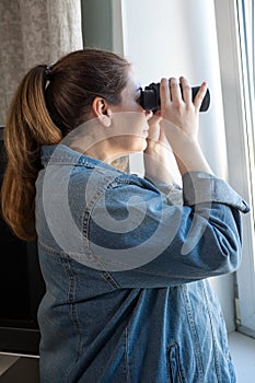 Portrait of woman with binoculars looking out the window, spying on neighbors, side view