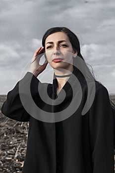 Portrait of woman in a black coat whose hair is flying in the wind stands in a field