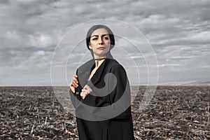 Portrait of woman in a black coat whose hair is flying in the wind stands in a field