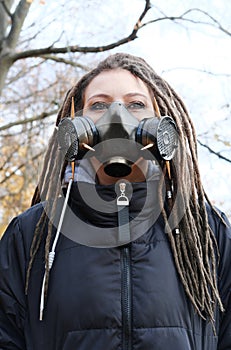 Portrait of a Woman in a black jacket with dreadlocks and a gas mask with spikes. Woman posing in autumn park