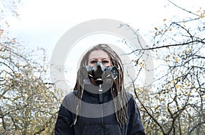 Portrait of a Woman in a black jacket with dreadlocks and a gas mask with spikes. Woman posing in autumn park