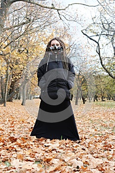 Portrait of a Woman in a black jacket and a long skirt with dreadlocks and a gas mask with spikes. Woman posing in