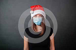 Portrait of a woman in a black T-shirt a disposable medical mask and a Christmas hat on a gray background