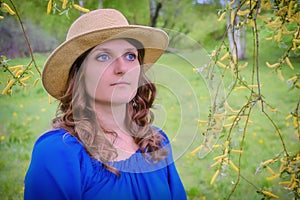 Portrait of a woman in a blue dress and hat on the background of a spring forest, copy space for text