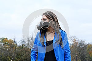 Portrait of a Woman in a blue jacket and dreadlocks in a gas mask with spikes.