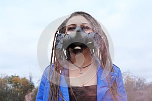 Portrait of a Woman in a blue jacket and dreadlocks in a gas mask with spikes. woman standing in smoke.